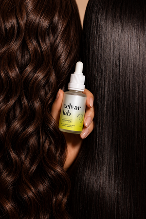 Mano sosteniendo el tónico capilar Zelvar Lab entre cabello ondulado y cabello liso